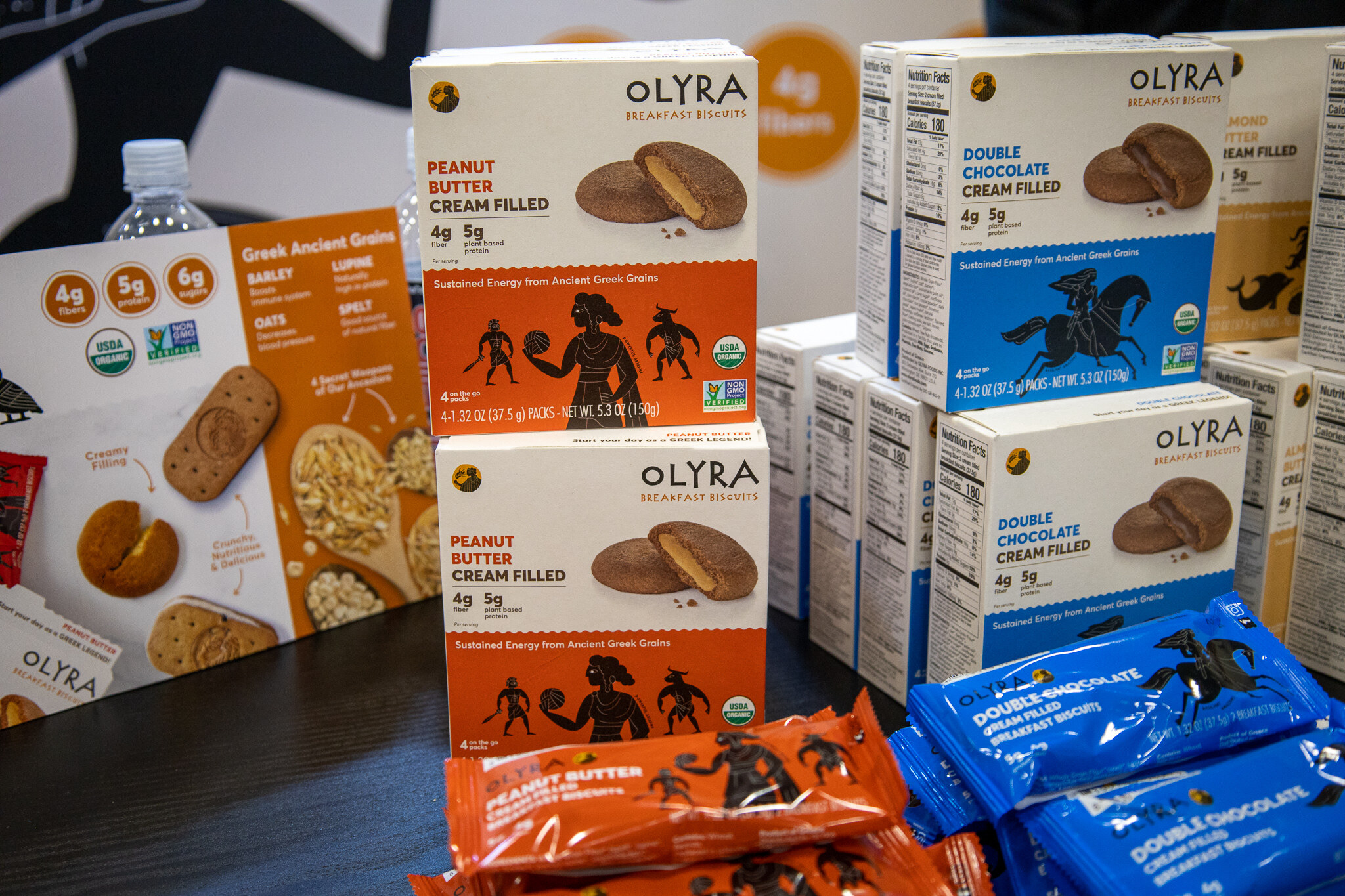 Boxes of Olyra breakfast cookies stacked next to a basket of snack bars