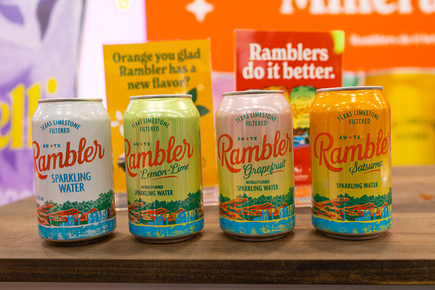 Four Rambler sparkling water cans in tall green and white designs on a wooden table