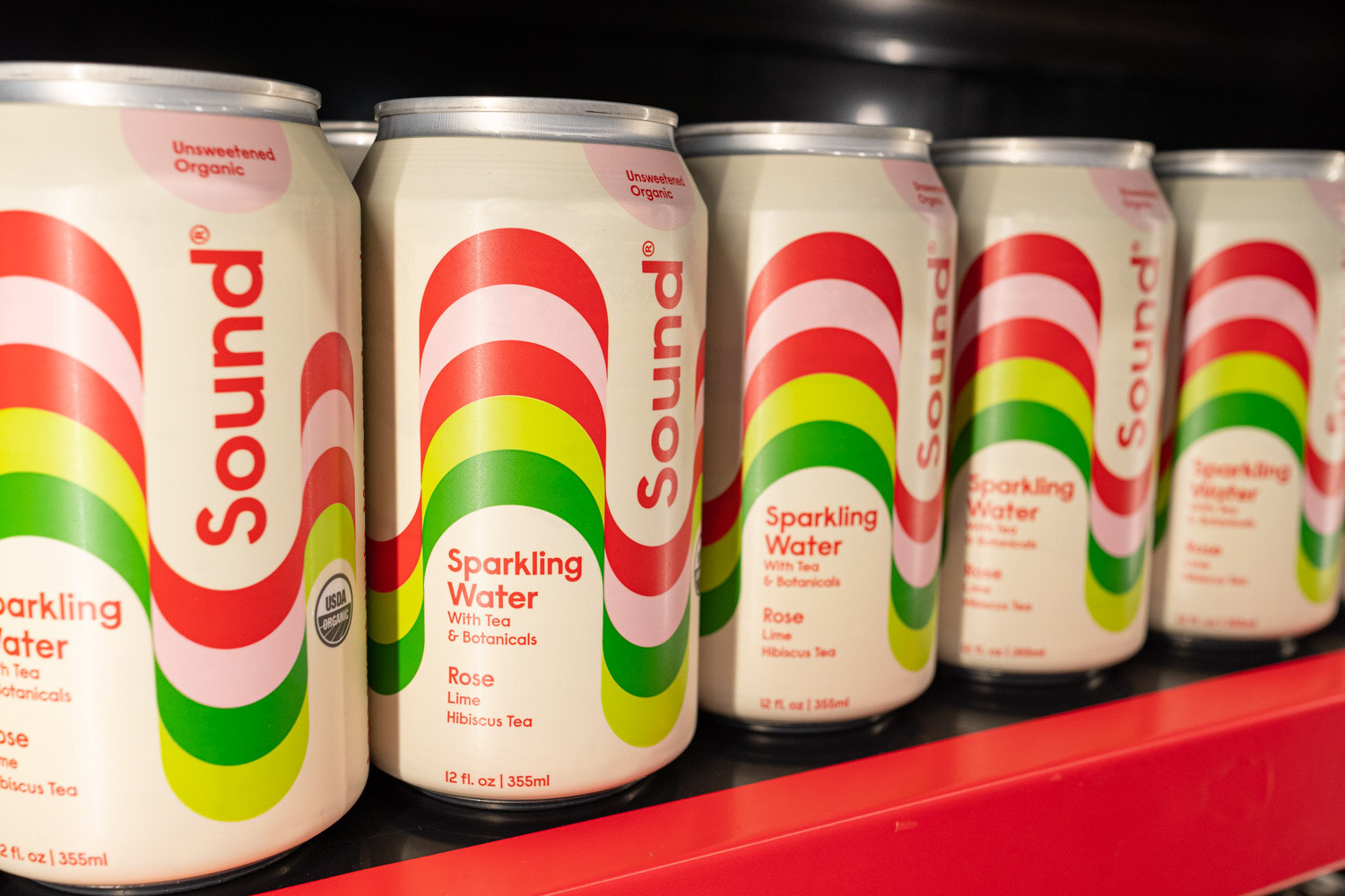 A row of Sound sparkling water cans with rainbow stripes on a red shelf