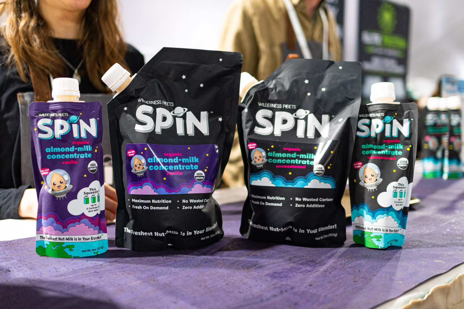 Spin almond milk concentrate pouches and small bottles standing on a purple table