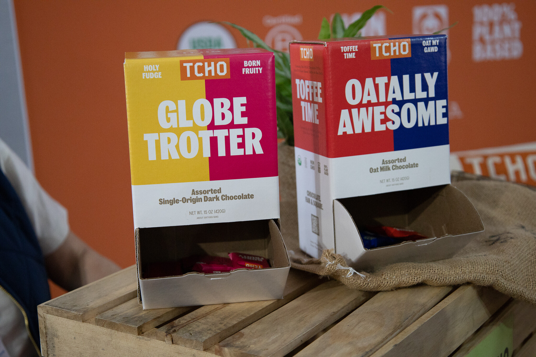Boxes of TCHO Dark and Salty and Hazel Nuts chocolate on burlap in front of an orange wall