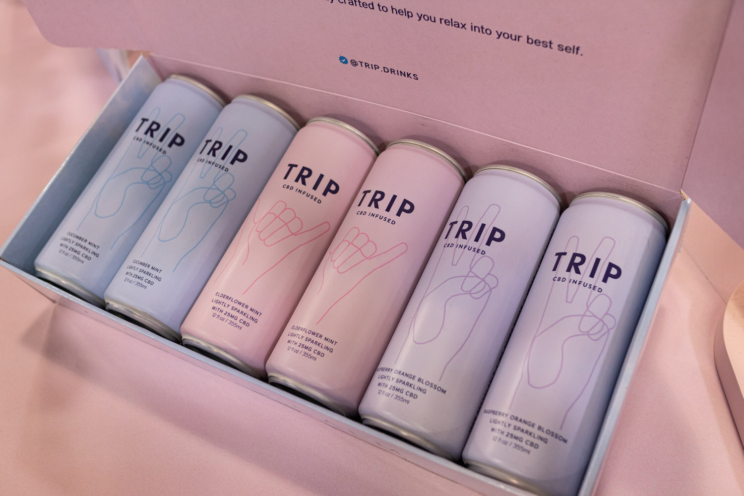 Five pastel Trip cans laid in a pink gift box