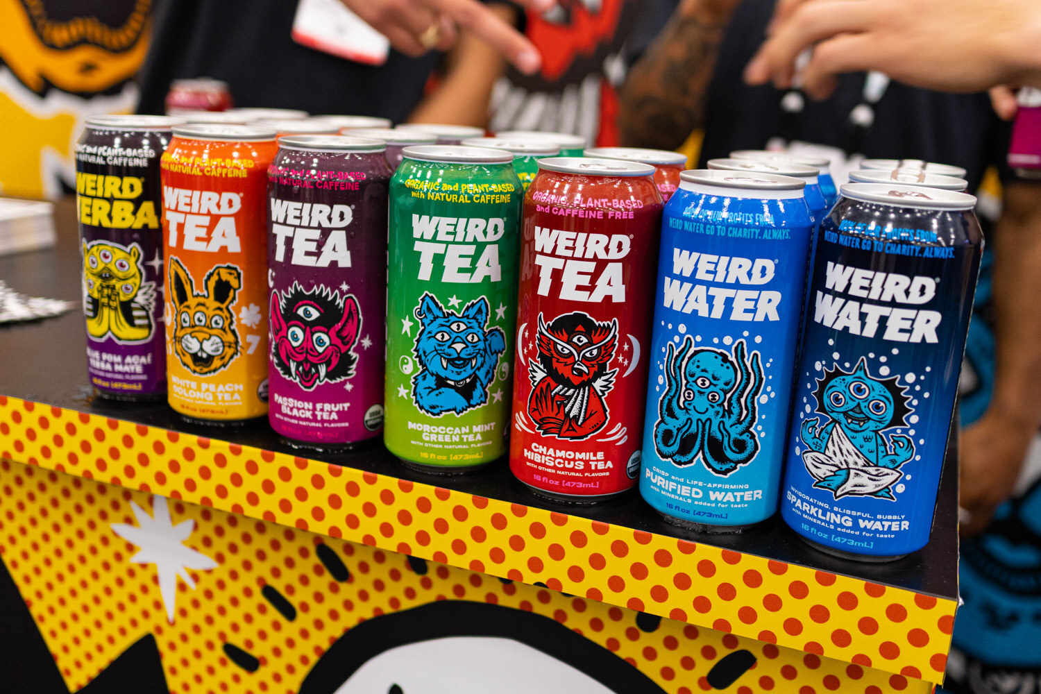 A row of Weird Tea and Weird Water cans on a polka-dot display
