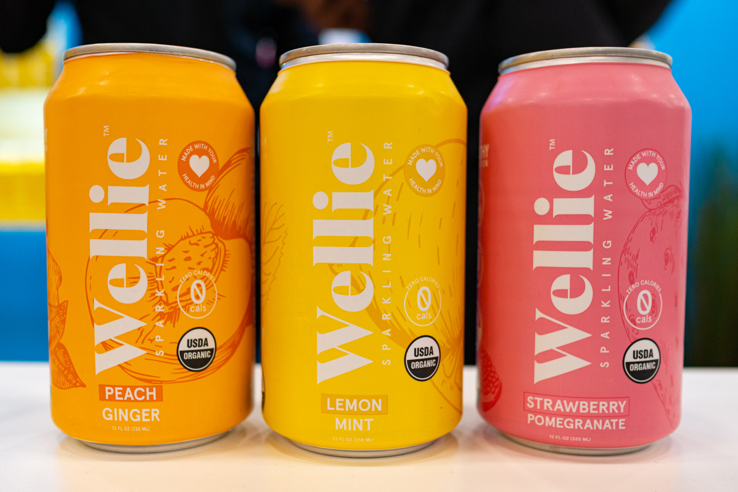 Three Wellie sparkling water cans in peach ginger, lemon mint and strawberry pomegranate