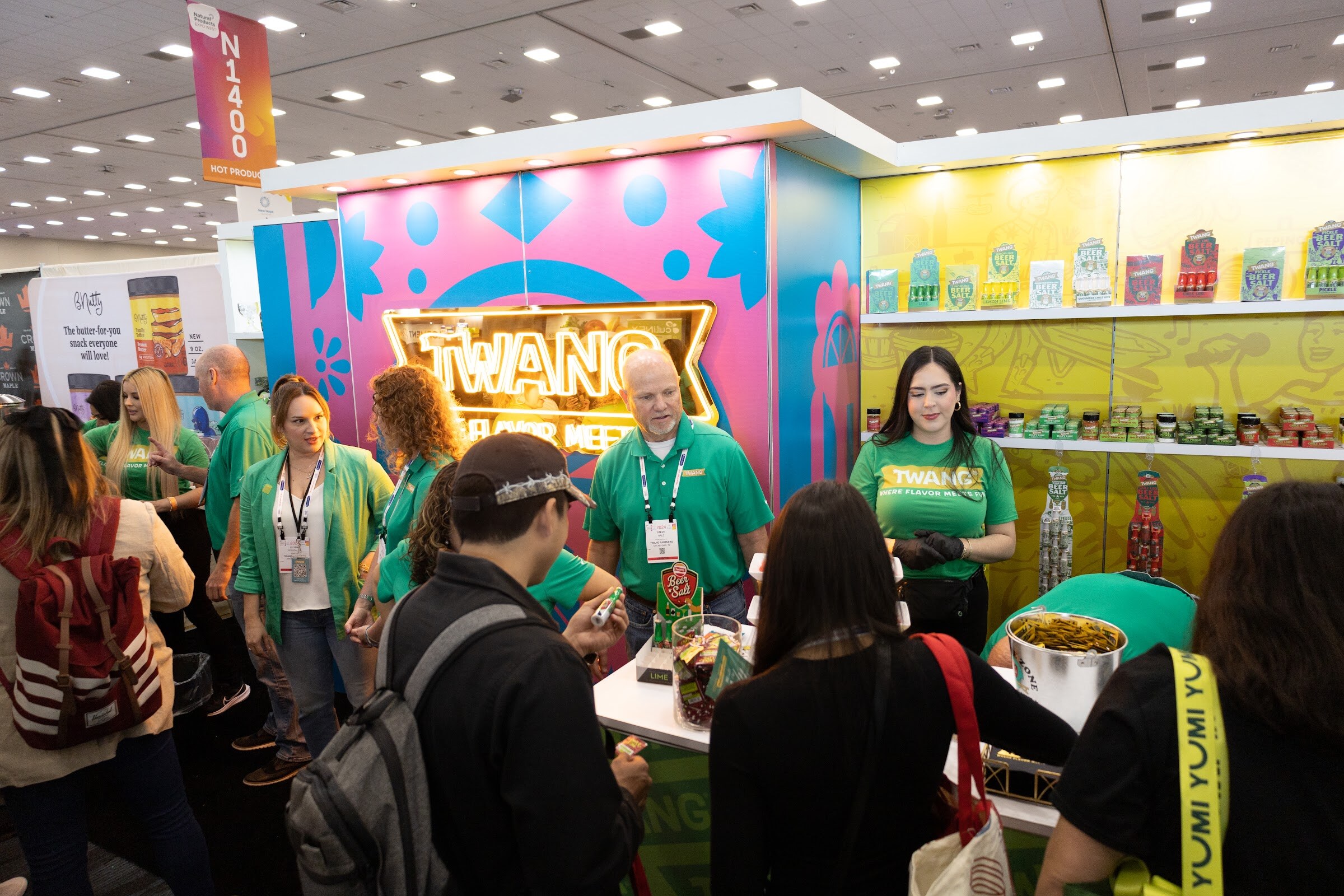 A crowd of attendees around a colorful booth where staff in green shirts are serving samples