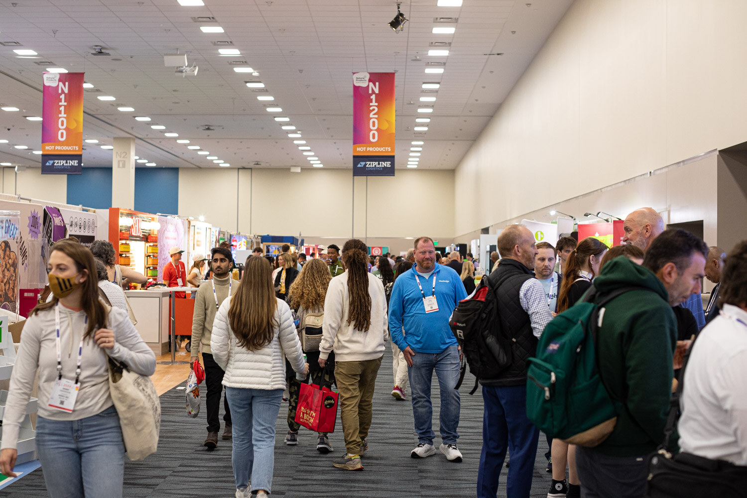 Attendees walking an aisle of an exhibit hall under hanging banners