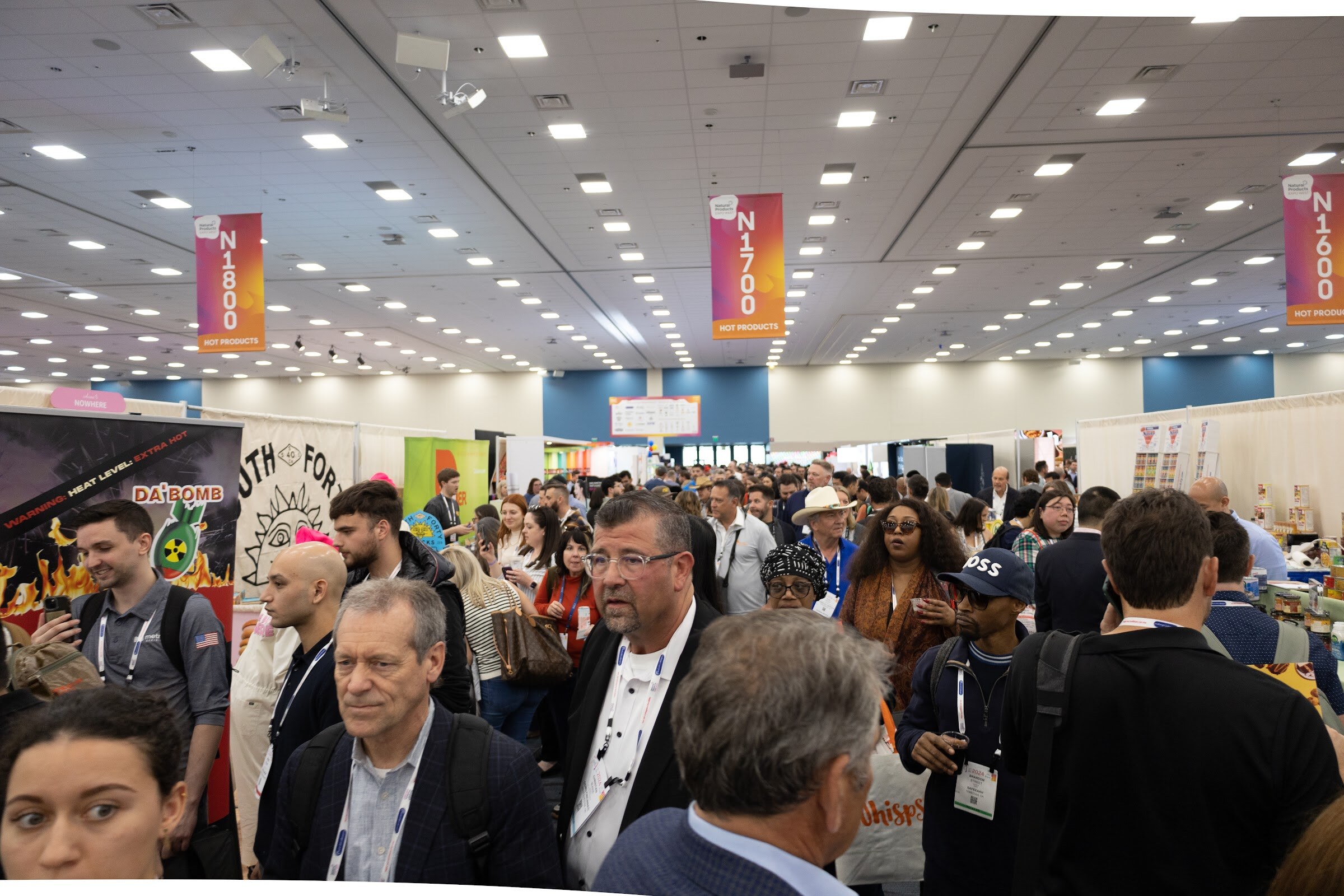 A dense crowd of attendees filling the aisles of the exhibit hall under overhead banners
