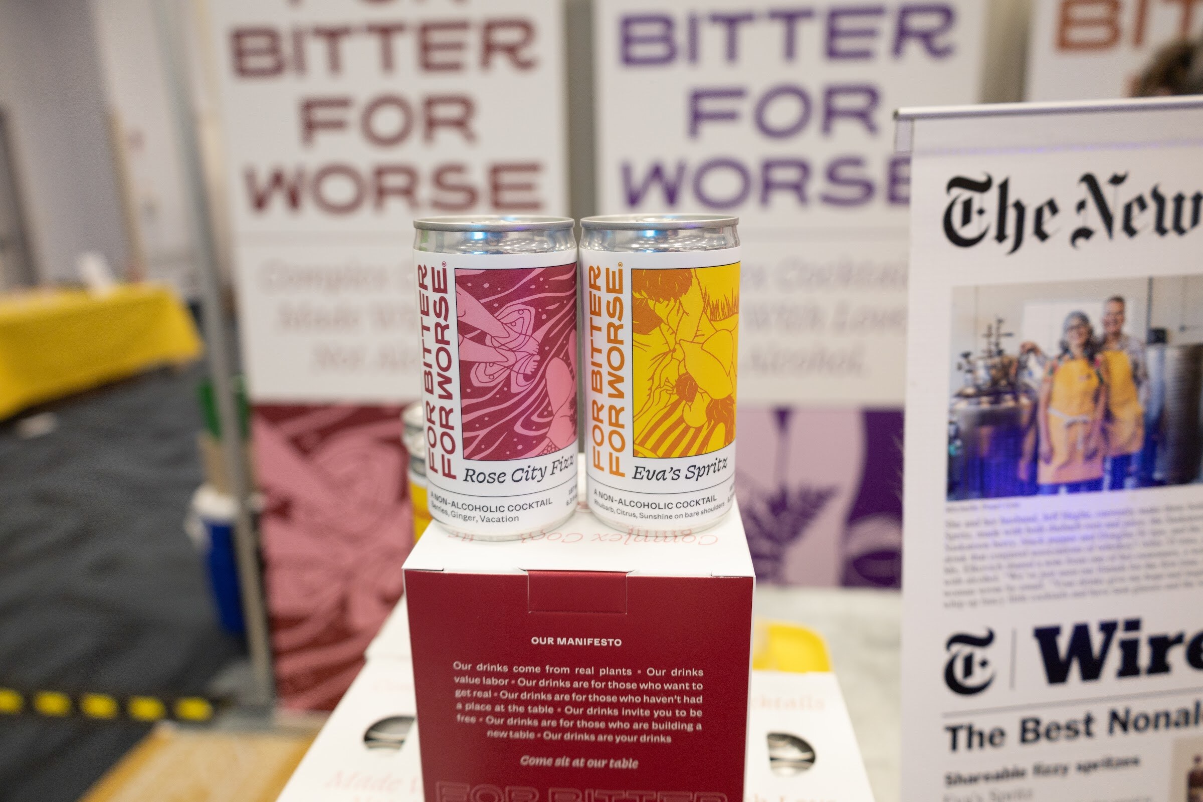Two Bitter for Worse cans on a box in front of the brand's banners and a newspaper article