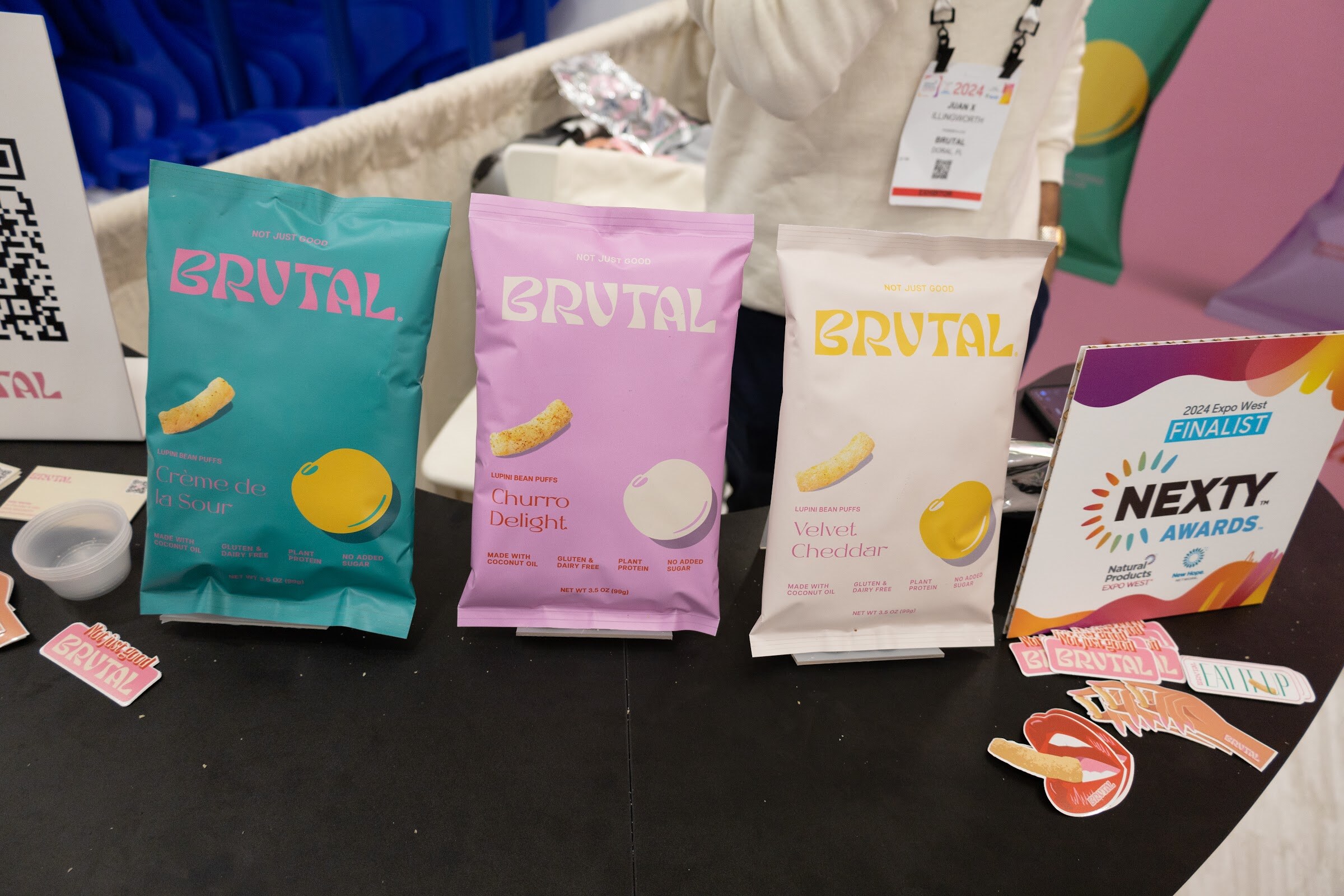 Bags of Brutal chips in teal, pink and cream beside a Nexty Awards Finalist sign