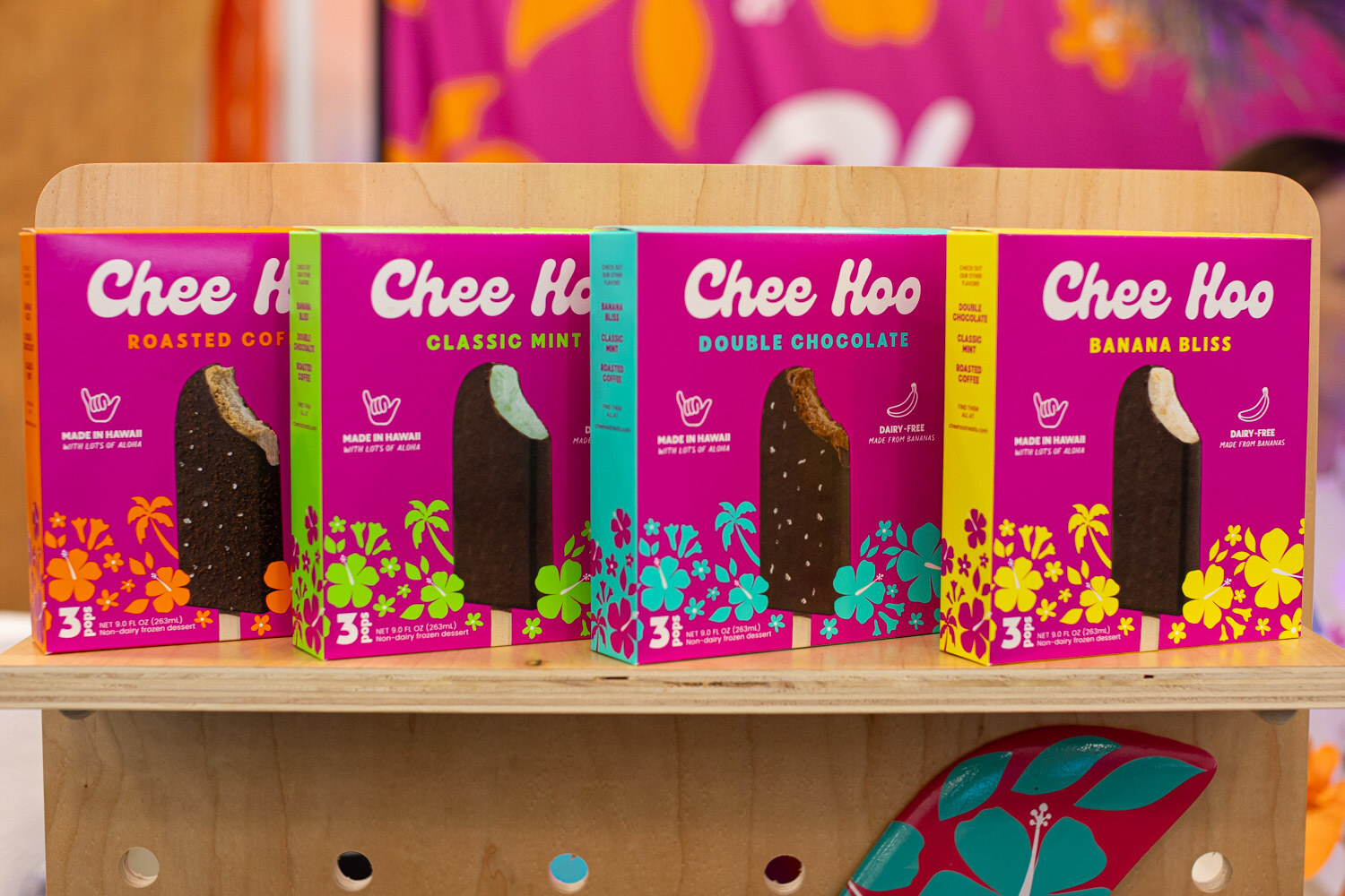 Boxes of Chee Hoo frozen bars in four flavors on a wooden stand with tropical patterns