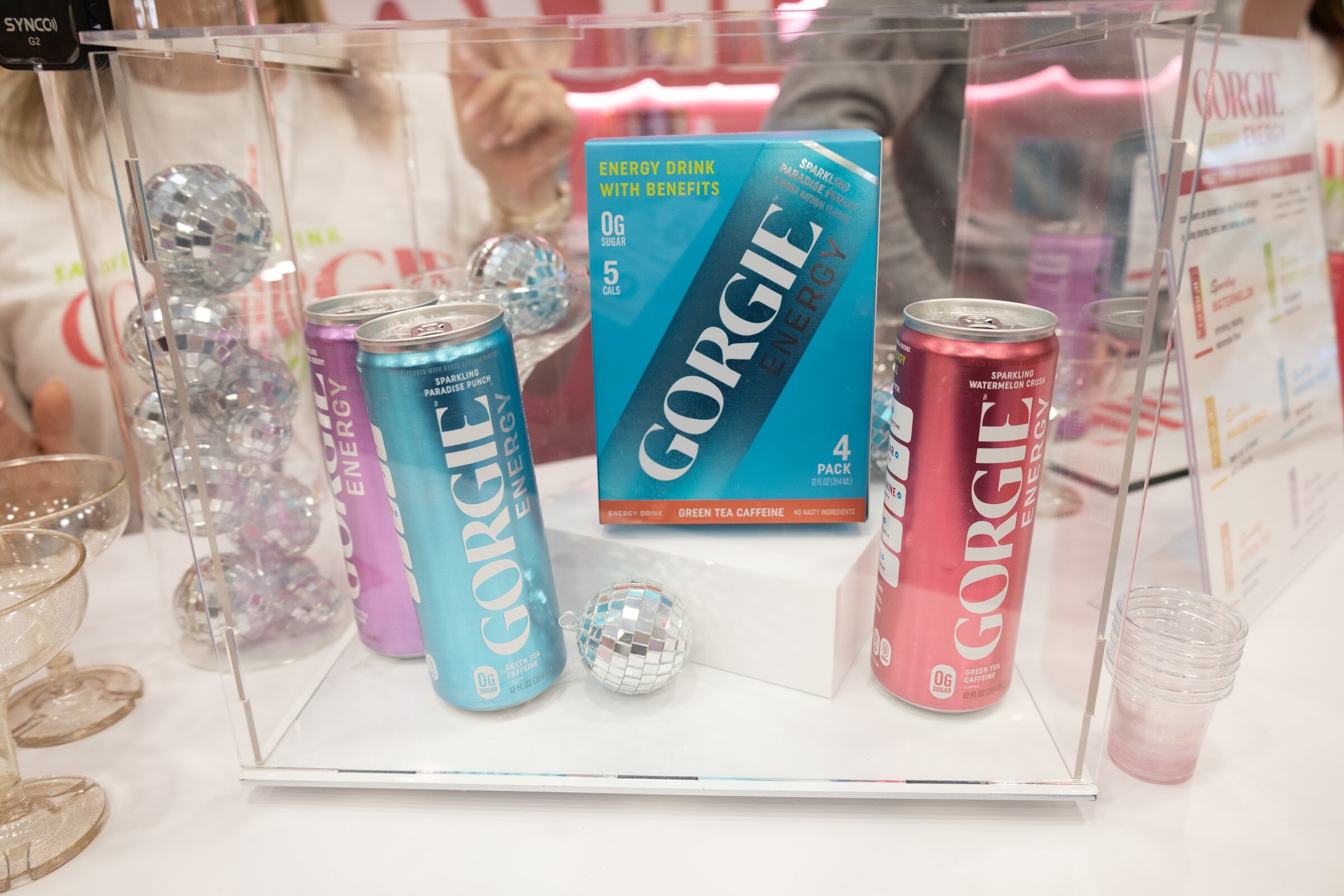 Gorgie energy cans and a four-pack in a clear display case with small disco balls