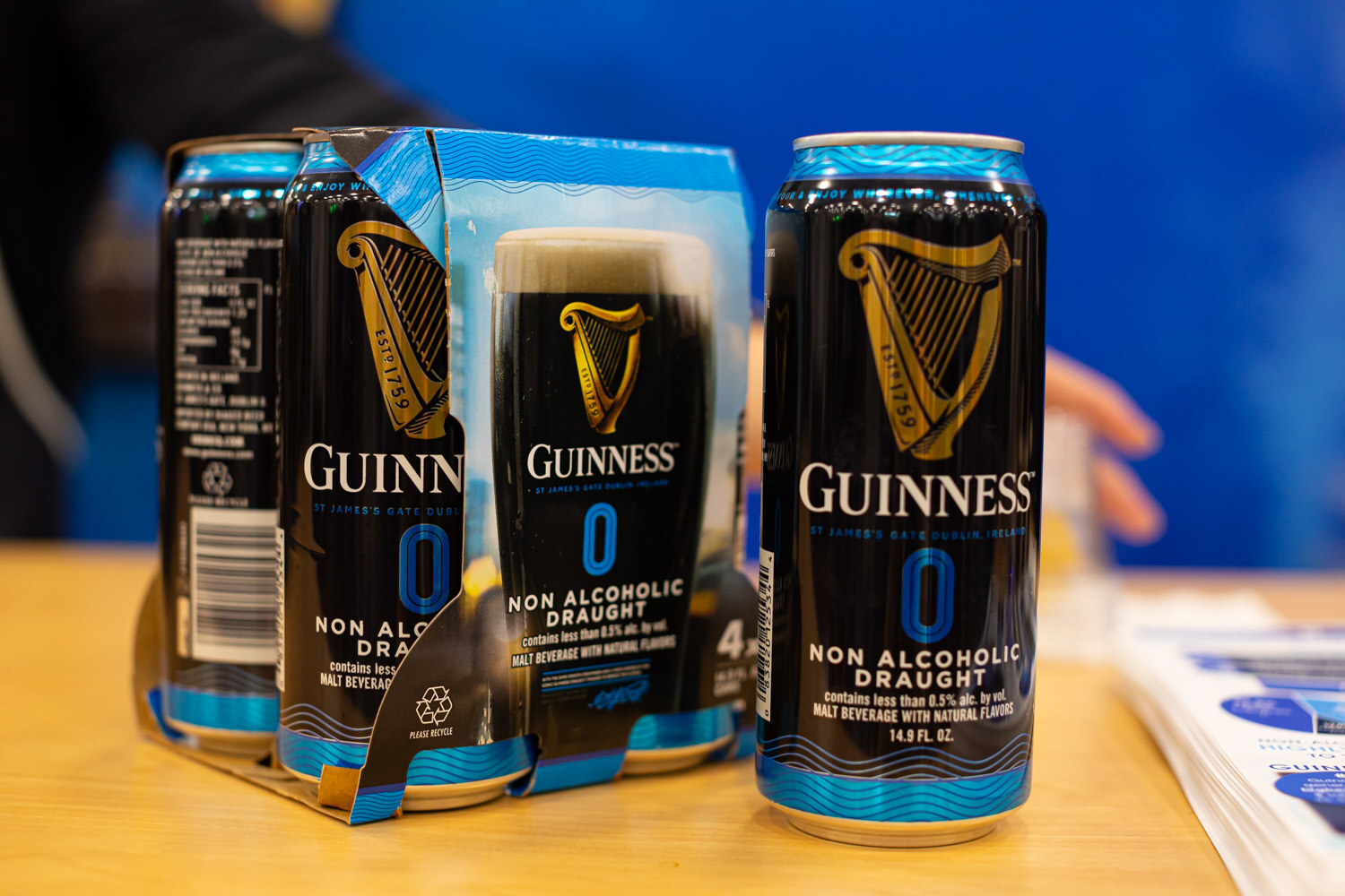 Guinness 0 non-alcoholic draught cans and a four-pack on a blue table