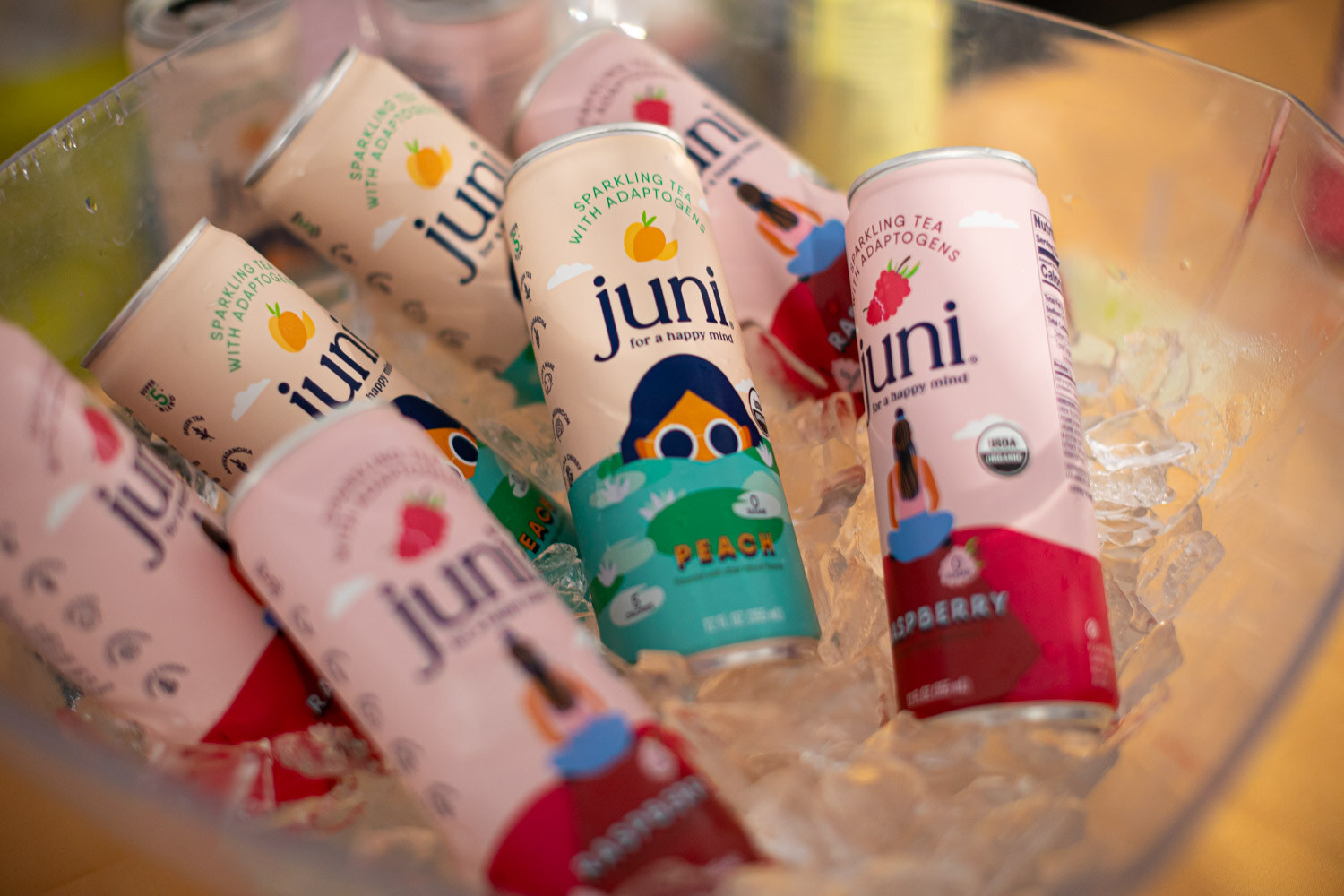 Juni sparkling tea cans in peach and raspberry flavors resting in a clear bowl of ice