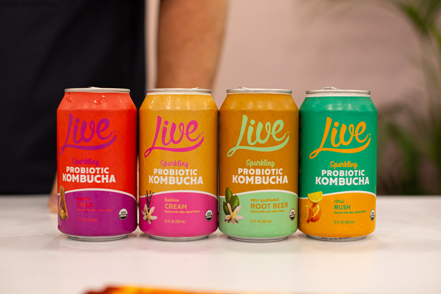 Four Live sparkling probiotic kombucha cans in different flavors lined up on a white table