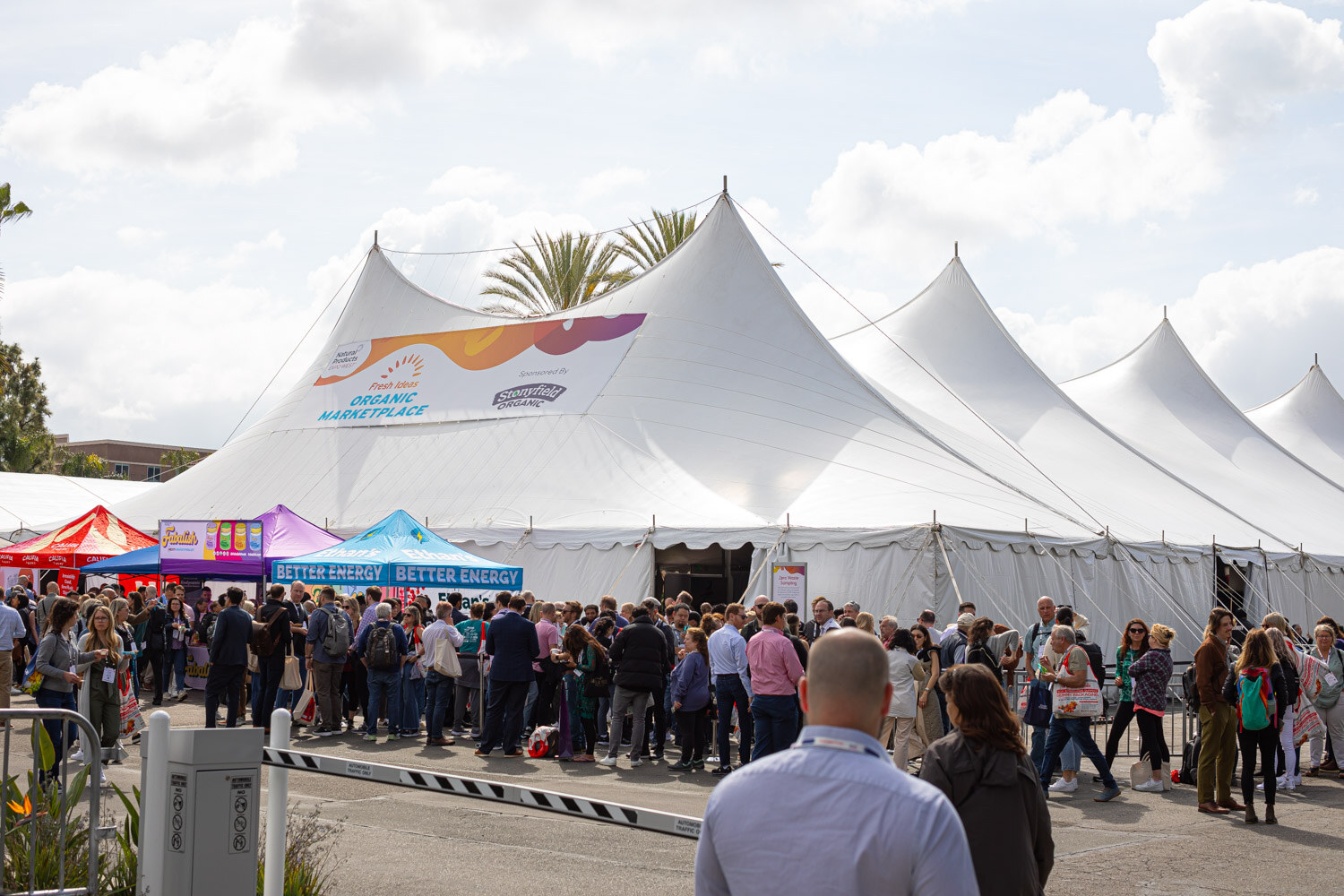 Attendees in line in front of large white tents with Organic Marketplace banners