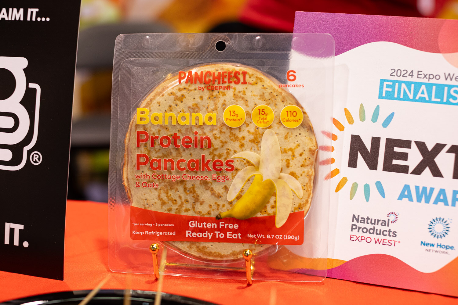 A Pancheesi banana protein pancake package next to a 2024 Expo West Nexty Awards finalist sign