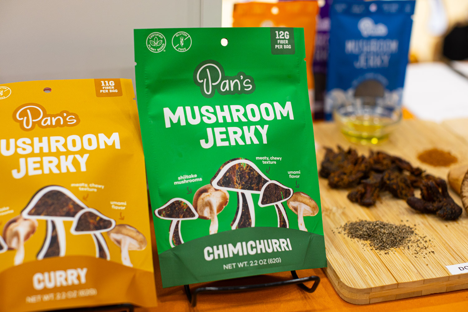 Bags of Pan's mushroom jerky in curry and chimichurri flavors on a wooden board