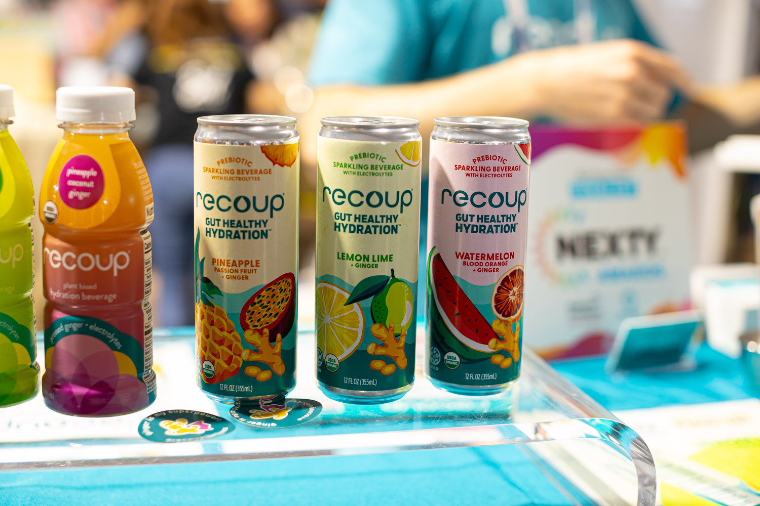 Recoup gut healthy hydration cans and a bottle on a teal table next to a Nexty Awards sign