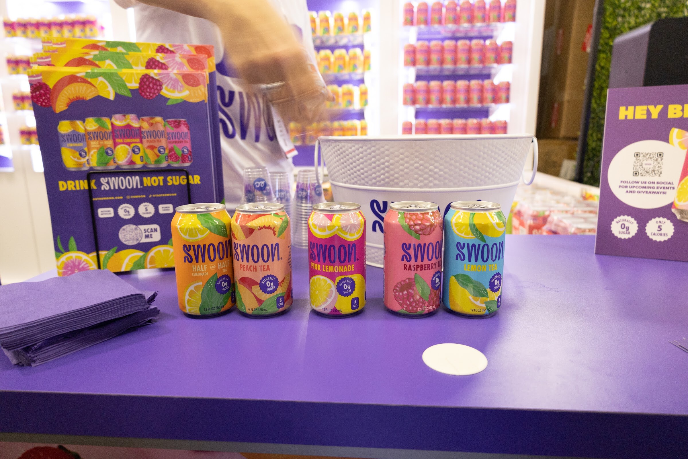 Five Swoon cans lined up on a purple counter in front of a Swoon booth display