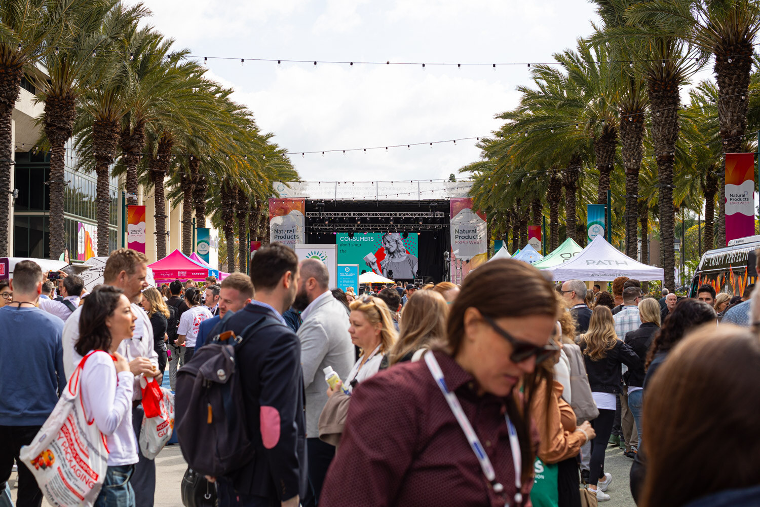 Attendees gathered on a palm-lined plaza with string lights and a stage at the far end