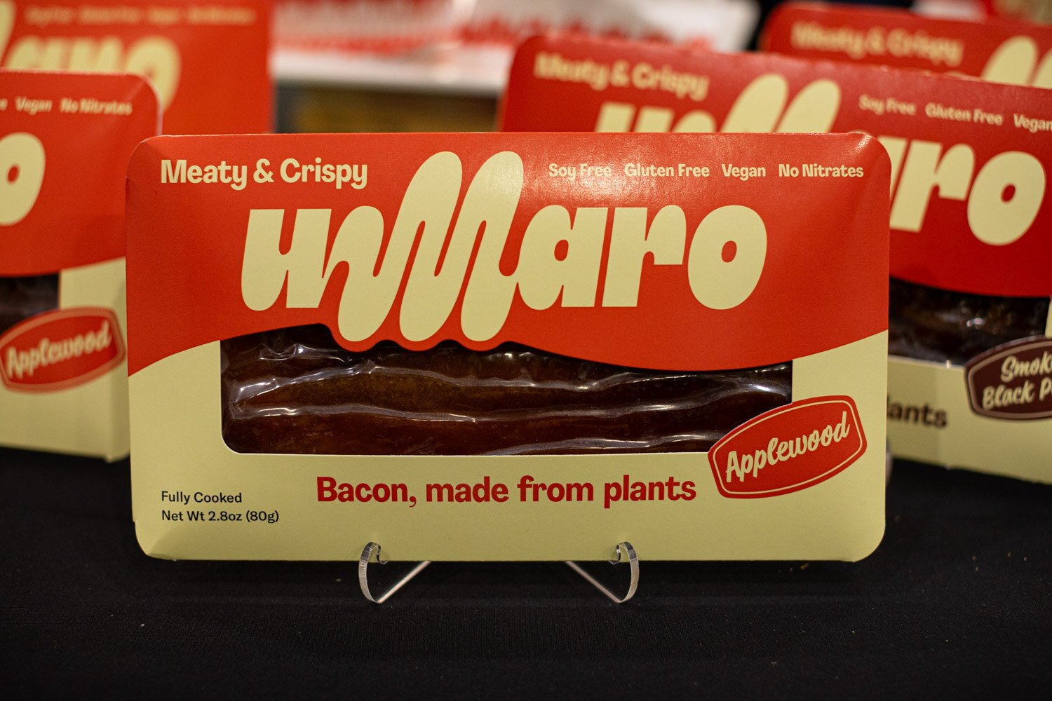 A pack of Umaro plant-based applewood bacon on a stand in front of more Umaro packages