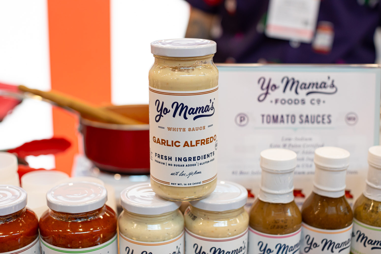 Jars and bottles of Yo Mama's Foods sauces including garlic alfredo and tomato sauces on a table