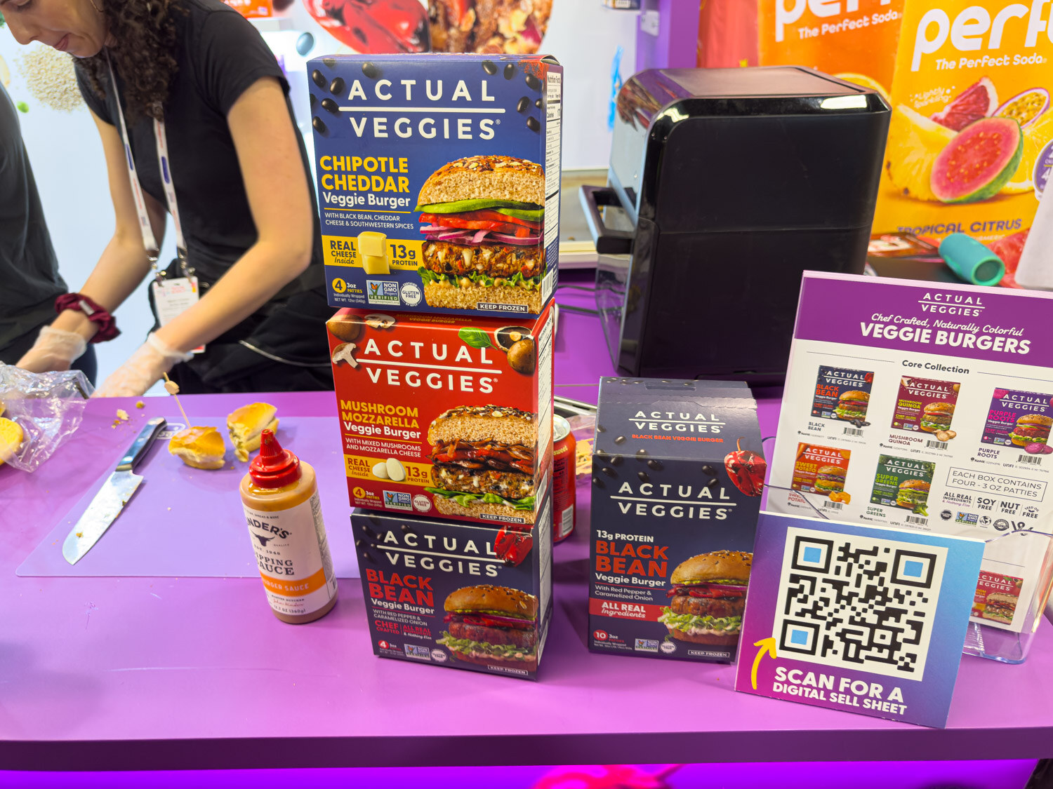 Actual Veggies burger boxes next to a person preparing samples and a QR code sign