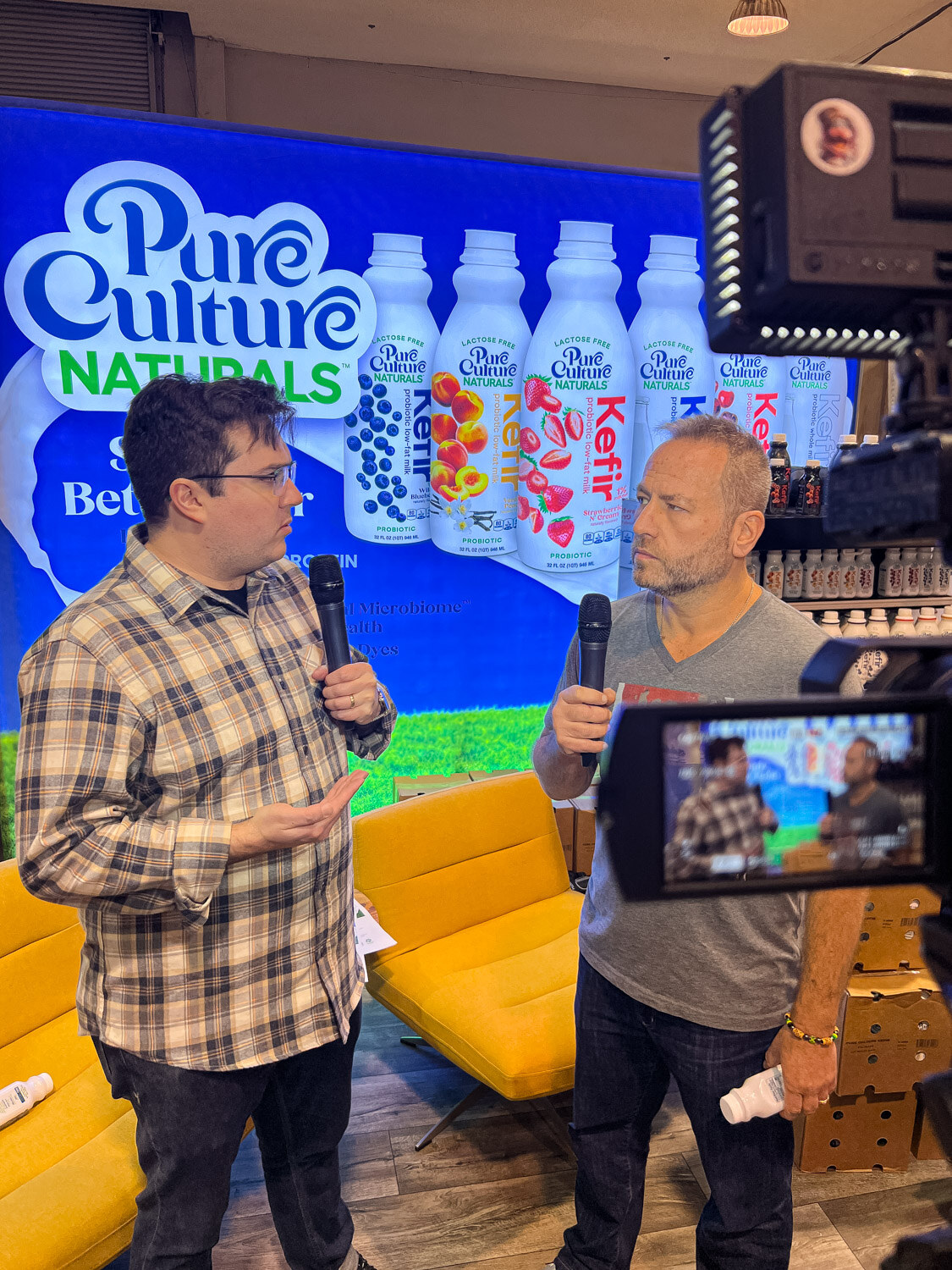 Two men being filmed with microphones in front of a Pure Culture Naturals backdrop