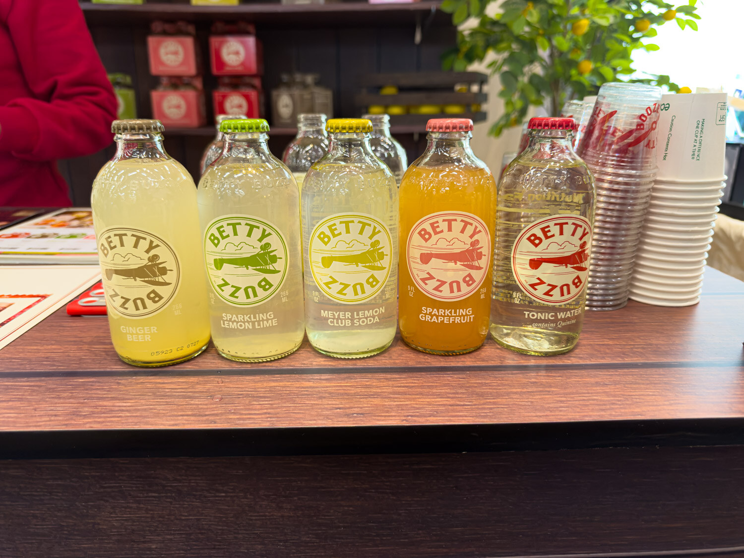 A row of Betty Buzz mixer bottles in lemon lime and grapefruit flavors on a dark wood counter