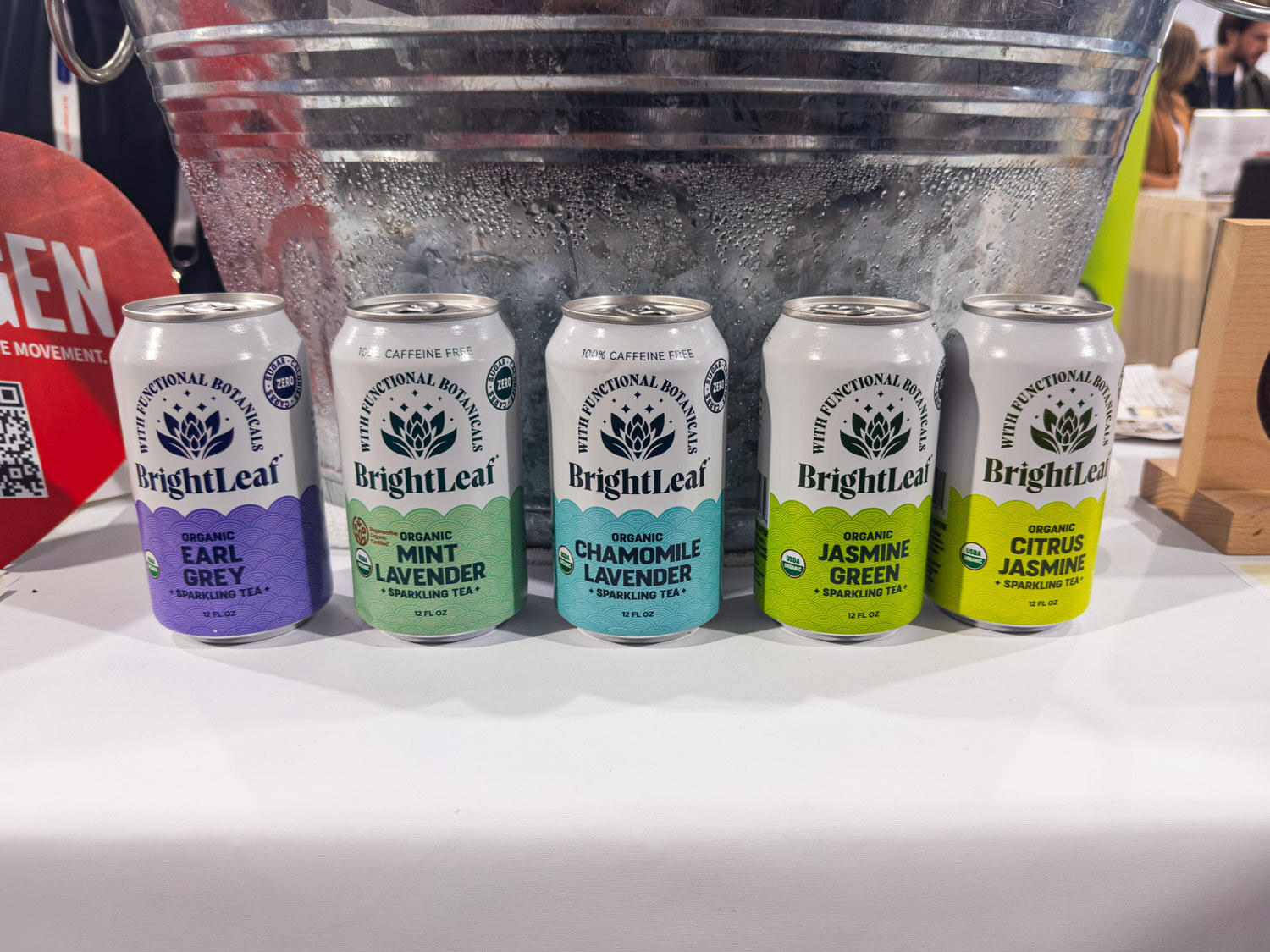 Five BrightLeaf sparkling tea cans in a row on a white tablecloth in front of a metal ice bucket