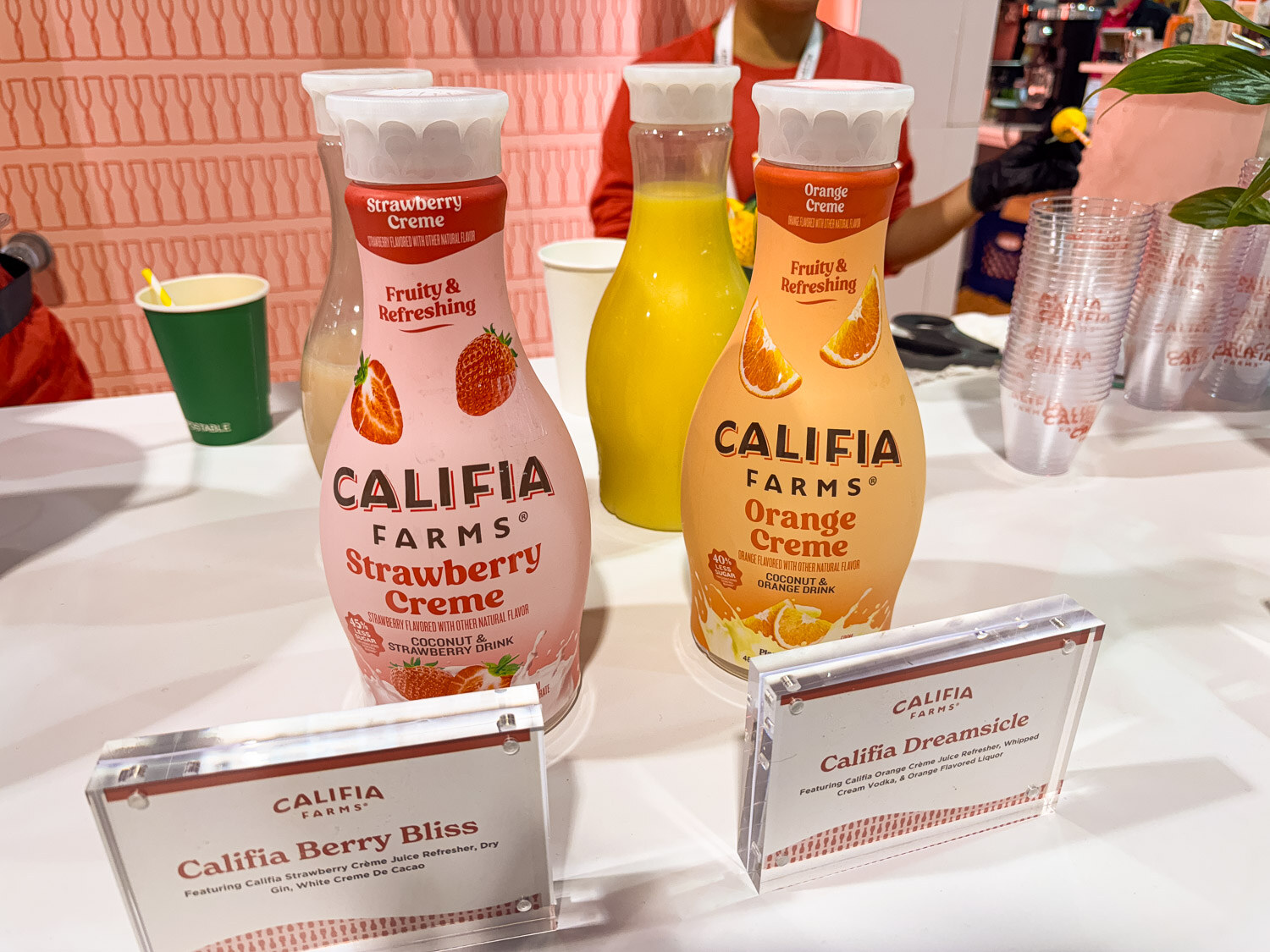 Califia Farms Strawberry Creme and Orange Creme bottles on a white table with small acrylic signs