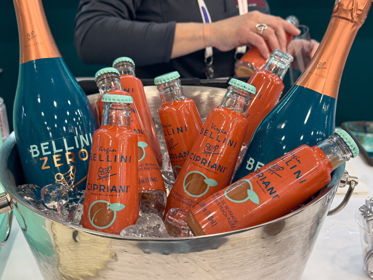 Cipriani Bellini Zero bottles and peach drinks in a silver ice bucket with a hand reaching in
