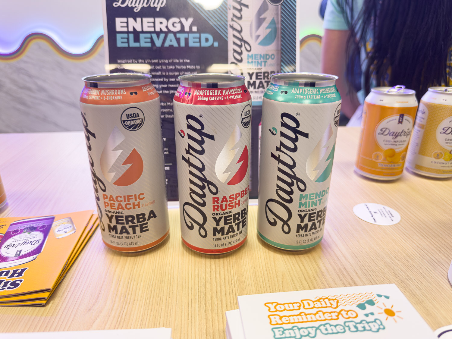 Three Daytrip organic yerba mate energy cans in front of a Daytrip sign