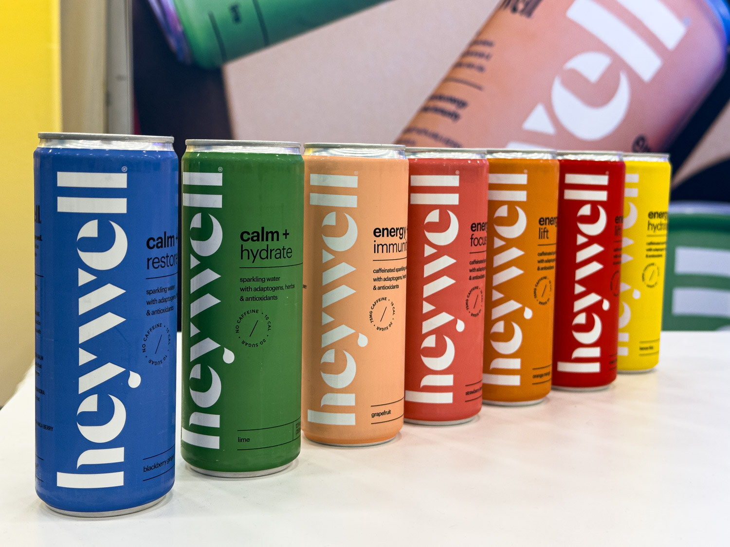 A row of Heywell cans in blue, green, orange, red and yellow on a white counter