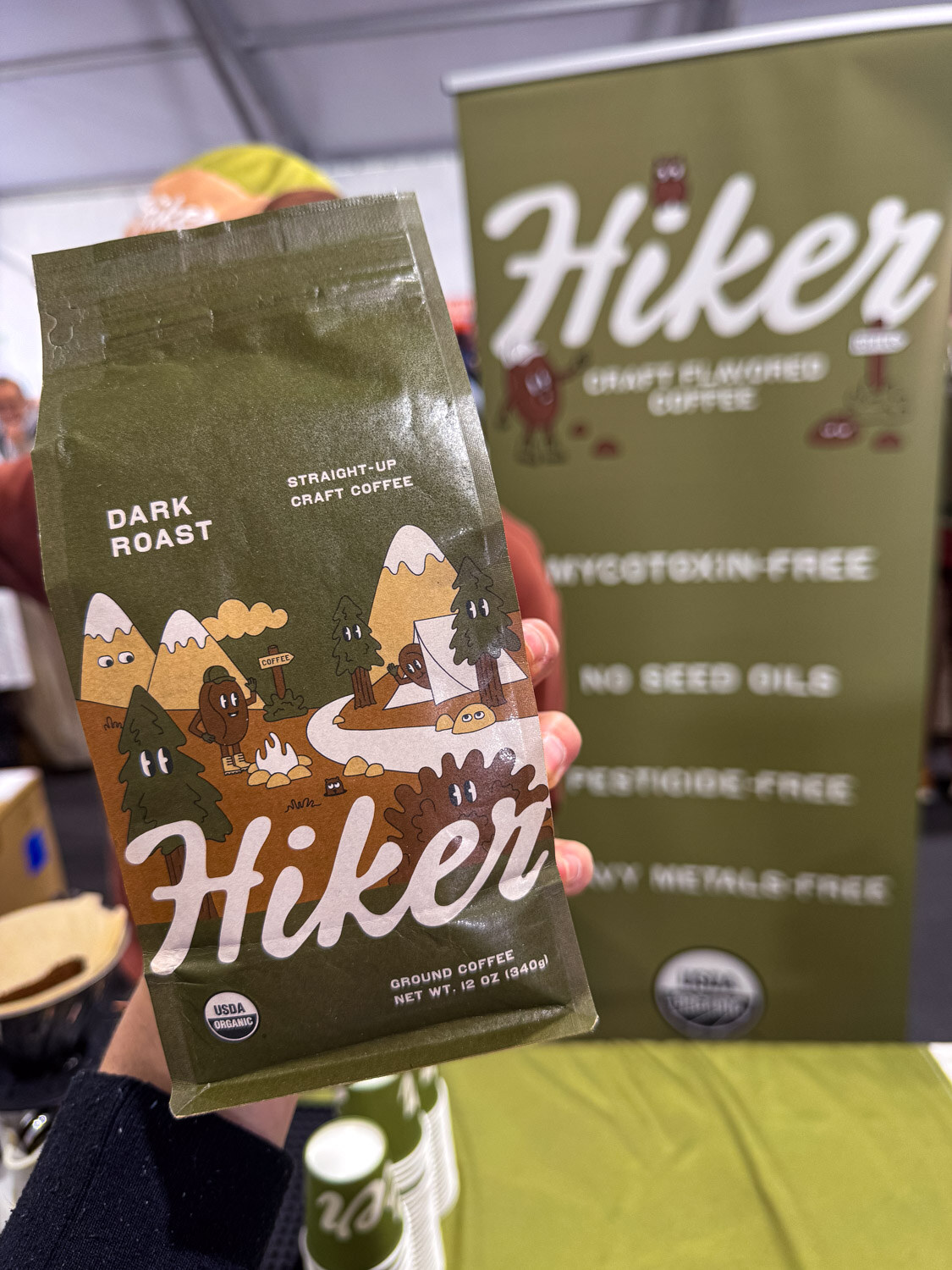 A hand holding a bag of Hiker dark roast coffee in front of a Hiker banner