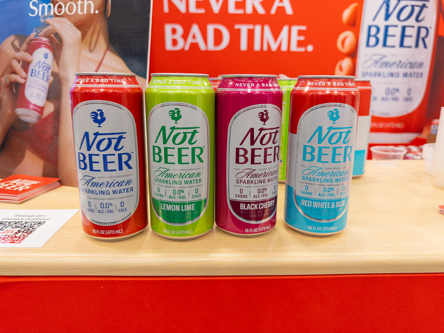 Four Not Beer sparkling water cans in lemon lime, black cherry and red white and blue next to a red banner
