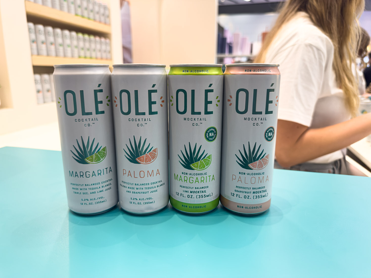 Four Olé margarita and paloma cans lined up on a teal counter