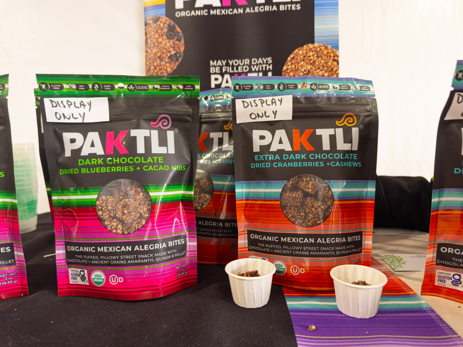 Bags of Paktli organic Mexican alegria bites with sample cups on a striped cloth