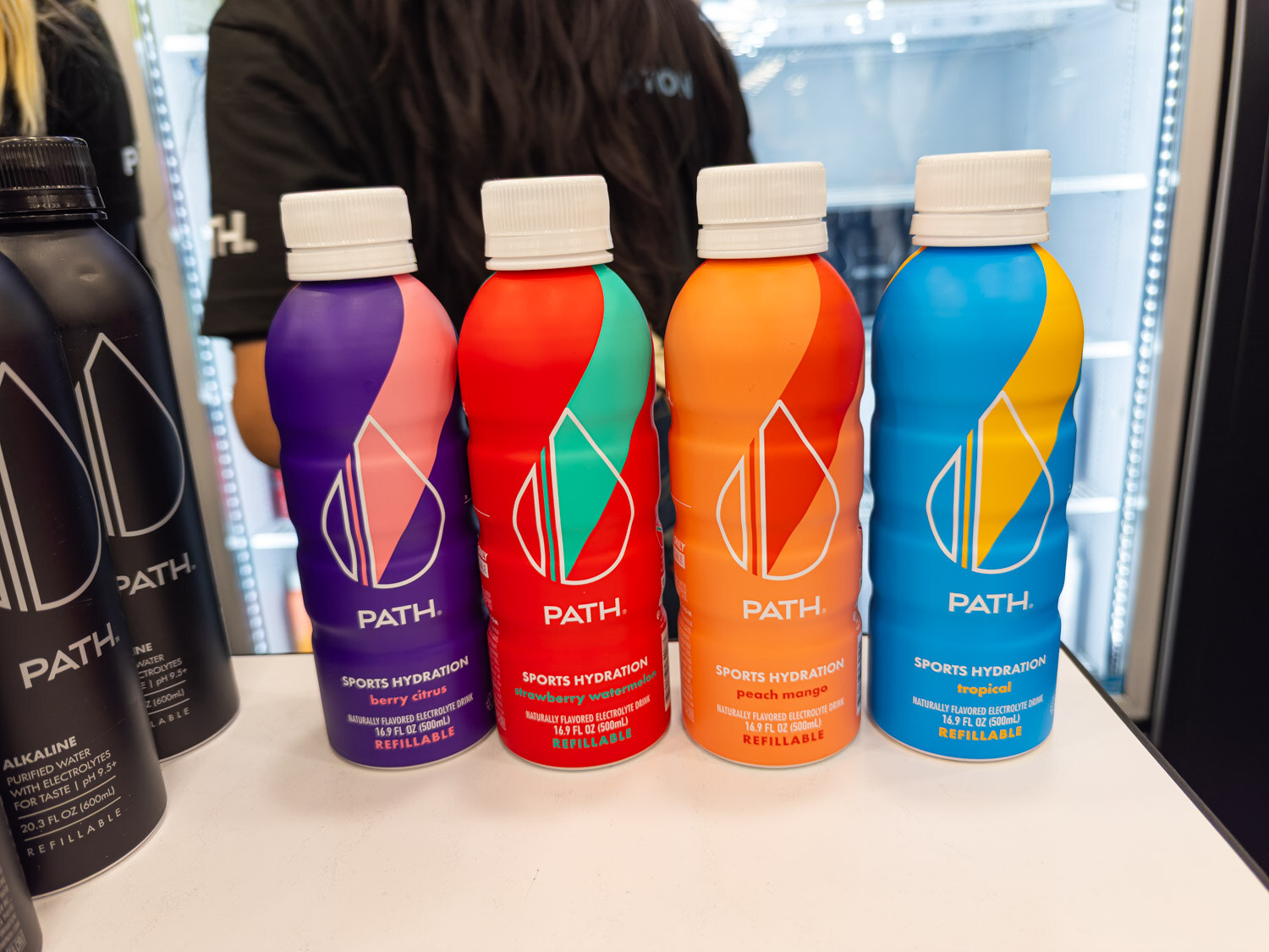Four colorful PATH sports hydration bottles lined up on a white counter