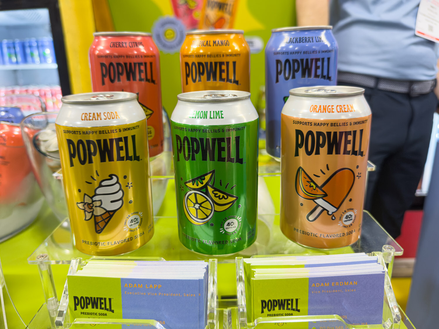 Three Popwell cans in cream soda, lemon lime and orange cream on an acrylic stand with business cards