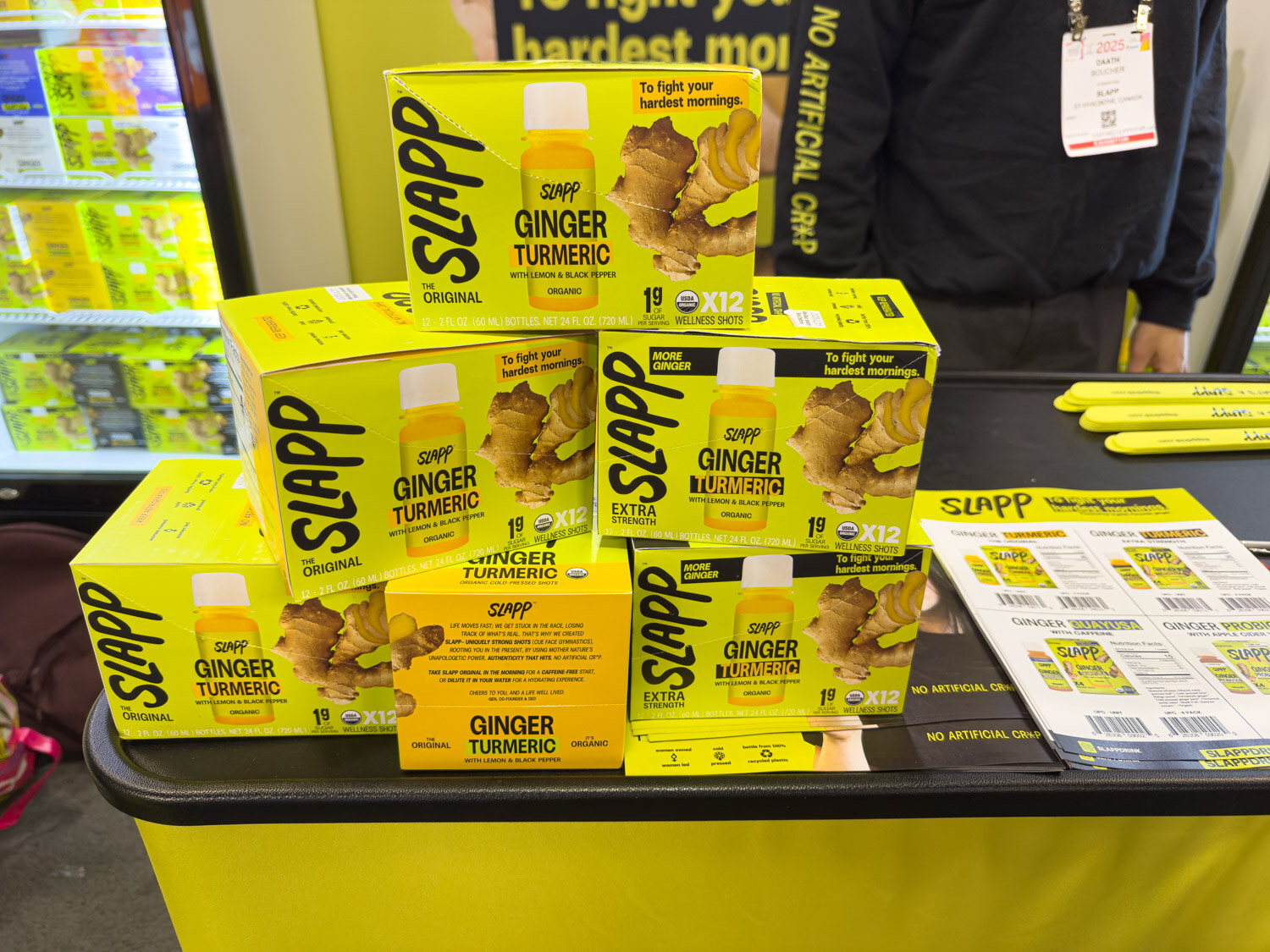 Stacked boxes of Slapp ginger turmeric wellness shots on a yellow counter