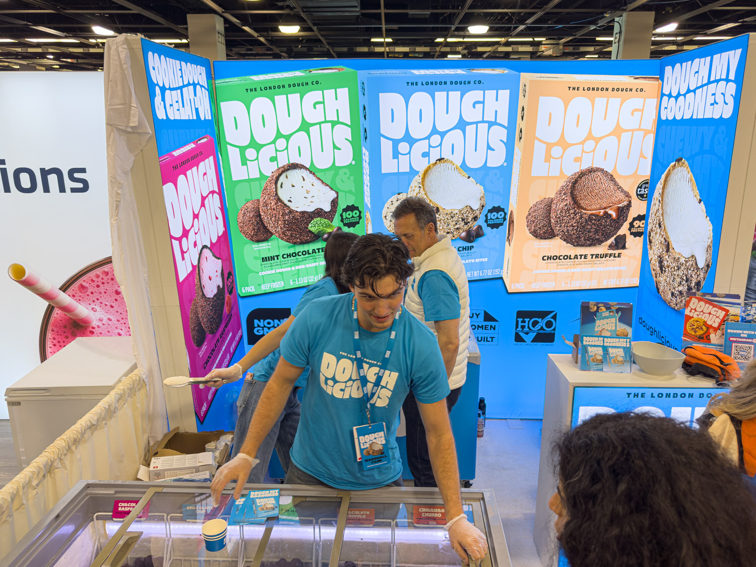 A person in a blue shirt leaning over a freezer case at a Dough Licious cookie dough booth