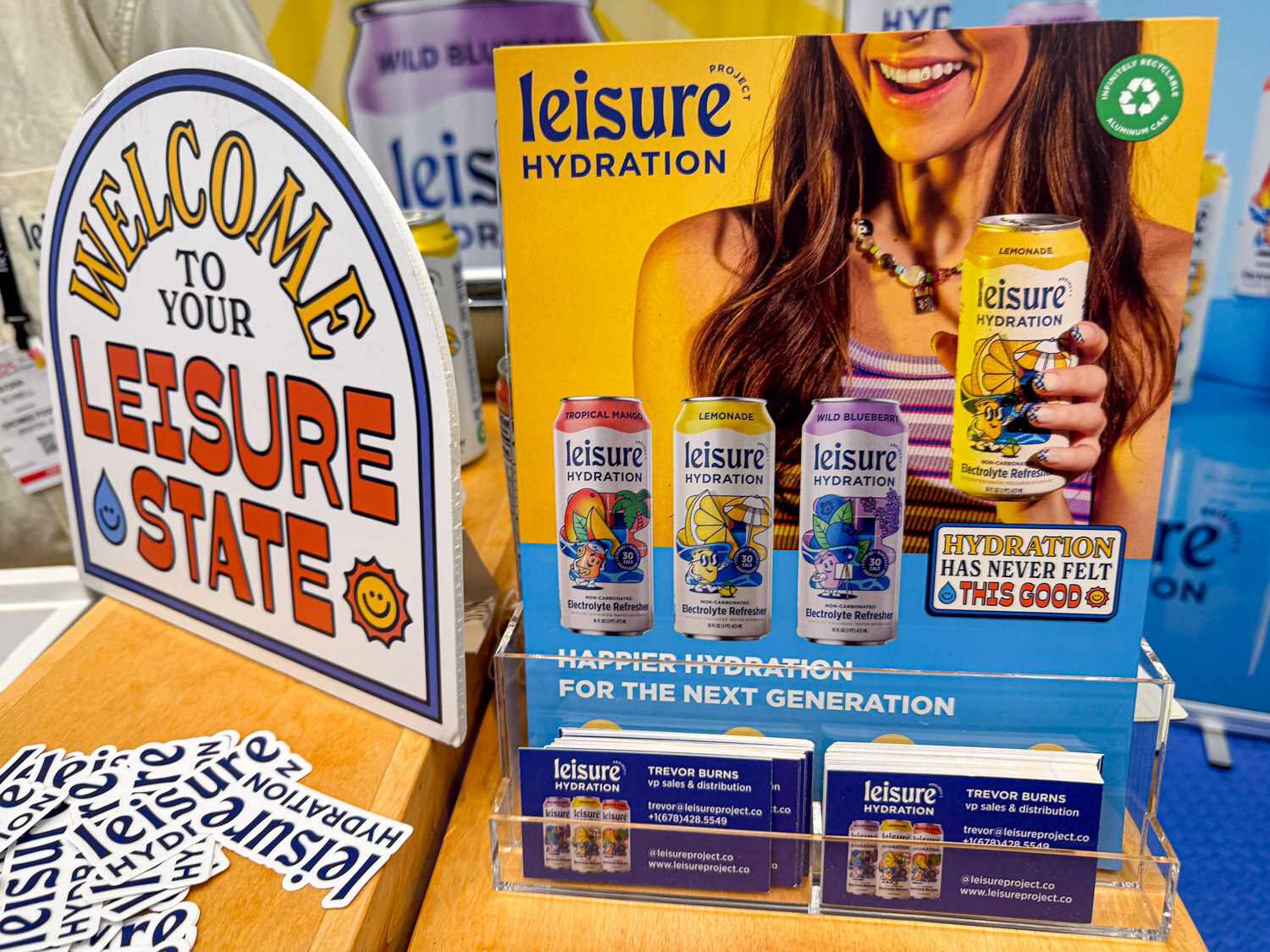 A Leisure Hydration booth display with a welcome sign and an ad with cans of electrolyte refresher