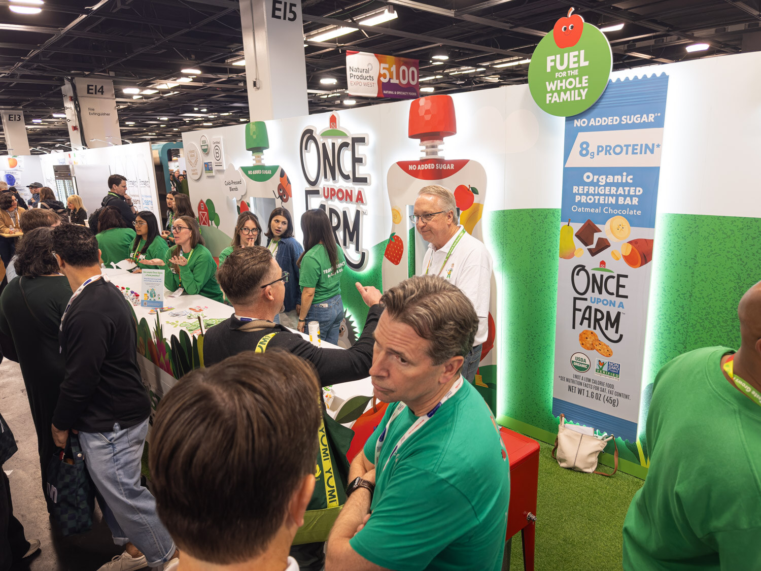 A Once Upon a Farm booth with a green display and a crowd of attendees at the counter