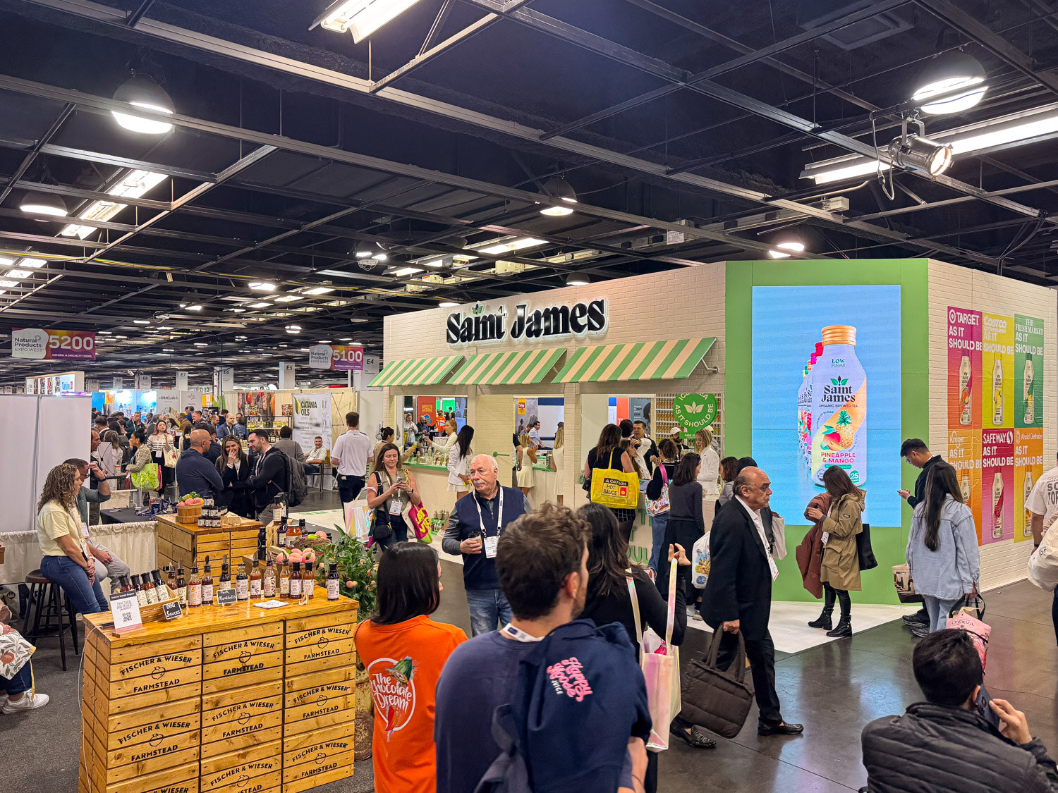 A Saint James booth with a green storefront-style display and attendees in the aisle