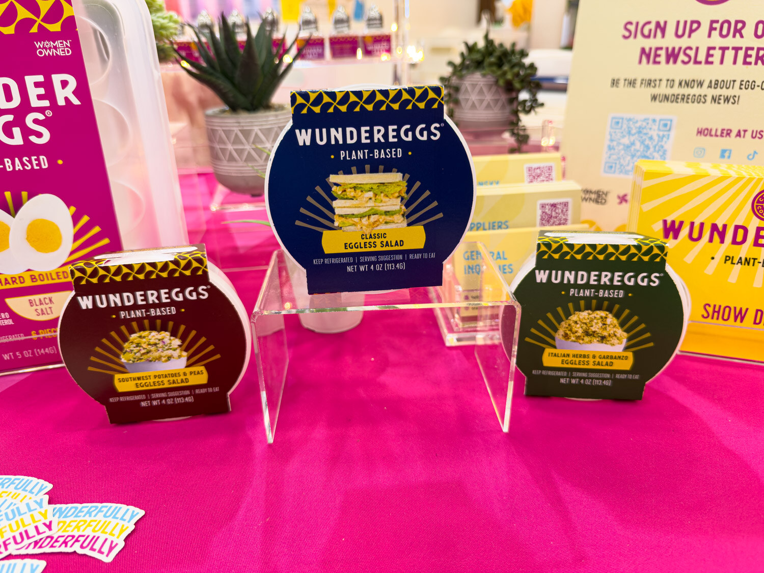 Wundereggs plant-based egg salad and sandwich products on acrylic stands on a pink table
