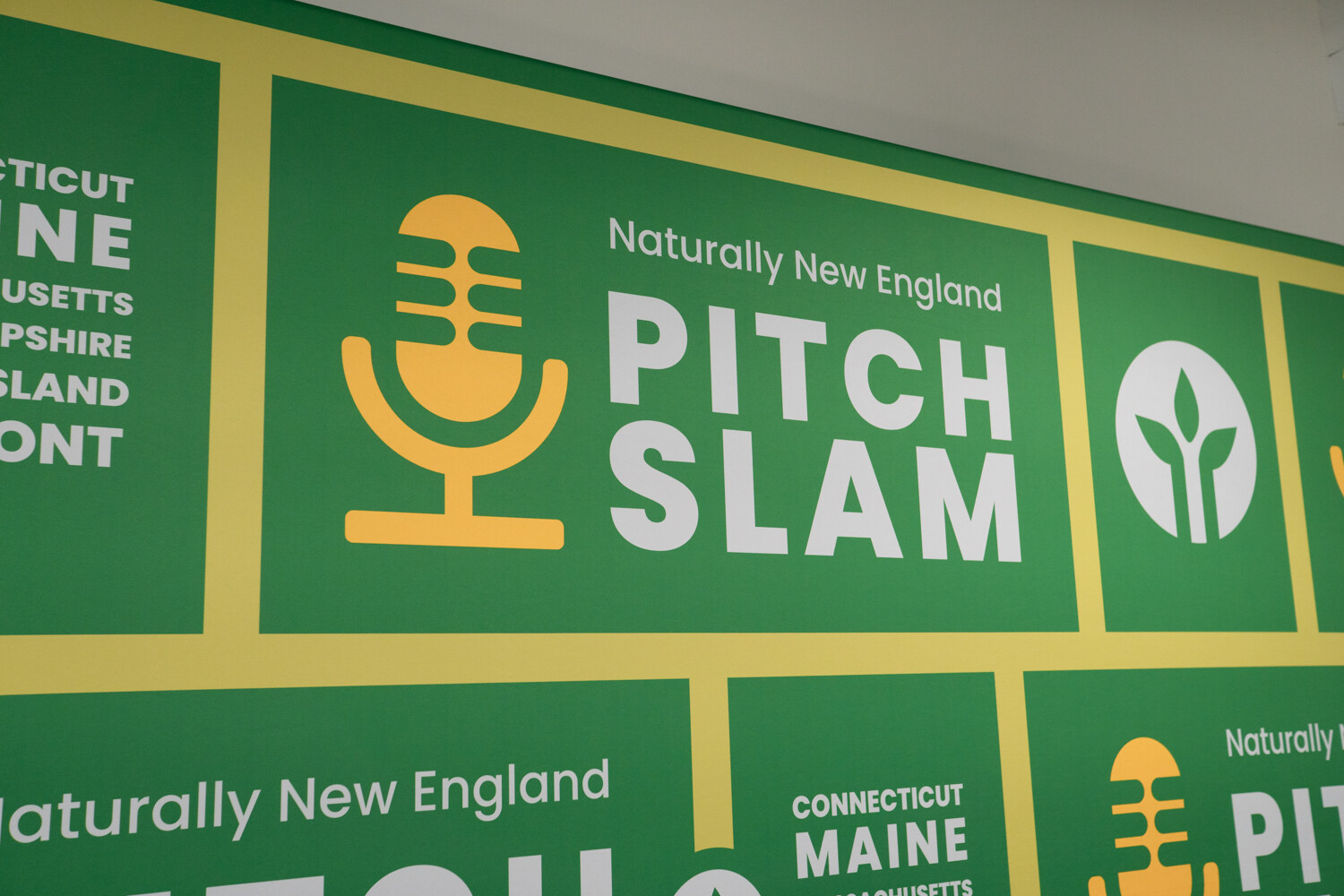 Close view of a green and yellow Naturally New England Pitch Slam banner with microphone and leaf icons.