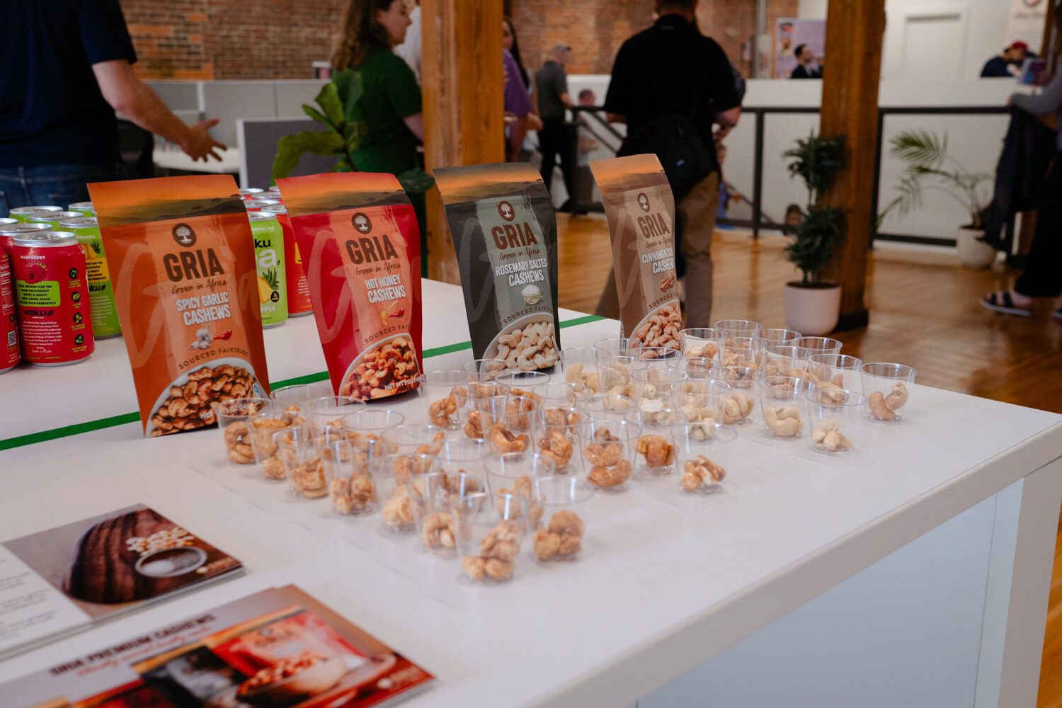Rows of small cups filled with cashew samples in front of orange and grey GRIA cashew bags.