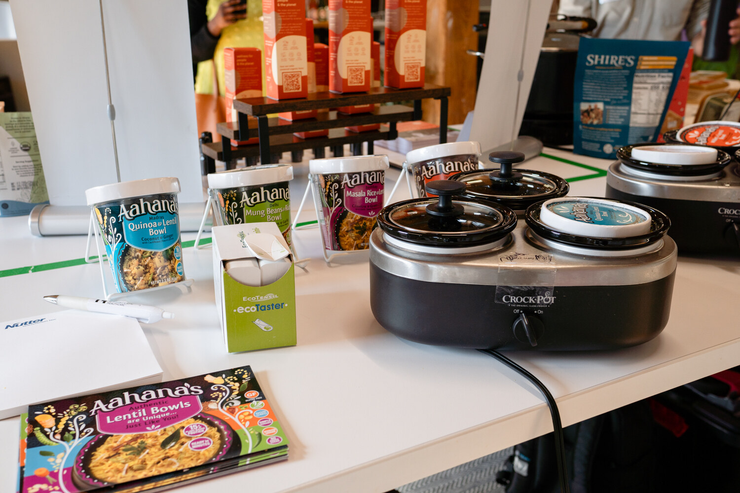 Aahana's lentil bowl cups and a recipe book next to a slow cooker on a white table.