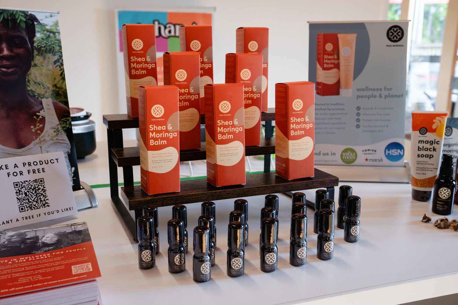 Orange boxes of shea and moringa balm stacked on a wooden riser above rows of small dark bottles.